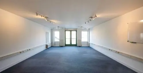 Lichte, lege kantoorruimte aan de Hoogte Kadijk met blauwe vloerbedekking en grote ramen aan het einde.